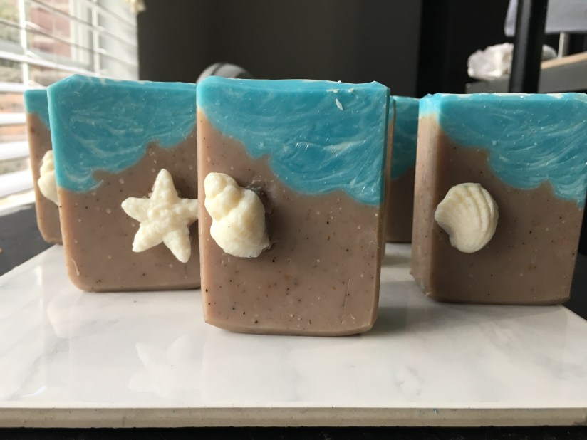 Brown soap bars with blue water effect simulation a beach and featuring a white shell embed on the sand portion