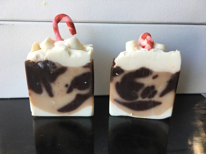 Handmade soaps with a dark and light shade of brown swirled. White tip with marshmallow decorations and candy cane decoration embed on top